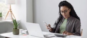 young African American woman looking at phone, calculator, and laptop