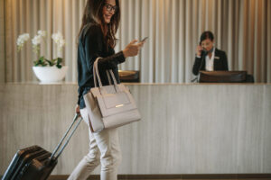 woman using mobile phone and pulling her suitcase in a hotel lobby